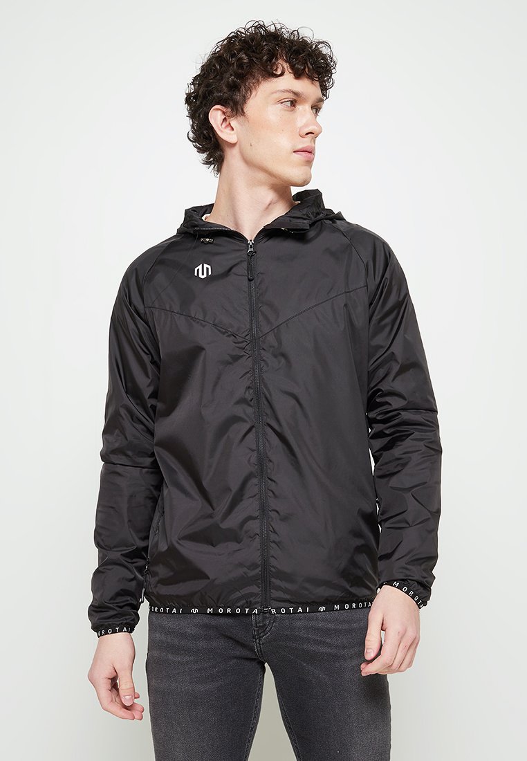 Veste légère noire avec capuche, fermeture éclair et logo blanc sur la poitrine. Présente des poignets élastiques et une ceinture à motifs.