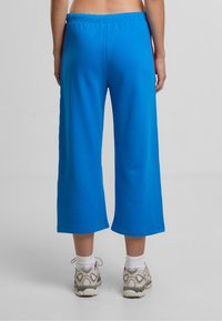 Kalhoty ve stylu culotte v jasně modré bavlně. Mají elastický pas a široké, zkrácené nohavice. Doplňují je béžové tenisky s vzorem.