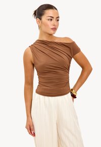 Bruine off-shoulder top met geplooide textuur; gladde stof; aansluitende silhoeet; gecombineerd met witte, gestreepte wijde broek.