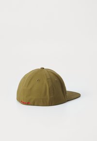 Khaki színű baseball sapka lapos karimával, szövettextúrával, hatpaneles kivitelben, és piros hímzett logóval a hátsó részen.