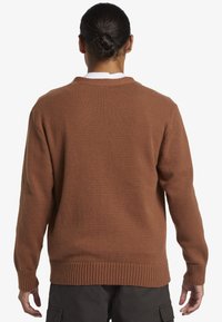 Brauner Strickpullover mit Rundhalsausschnitt, gerippten Bündchen und Saum, der eine strukturierte Oberfläche und ein raglanartiges Design aufweist.