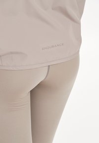 Ljust beige träningsleggings med en sömlös design och slät textur. "ENDURANCE"-logotypen syns subtilt nära midjebandet.