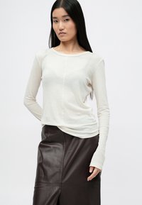 Długi rękaw kremowy top z lekkiego materiału, z okrągłym dekoltem i dopasowanym krojem, zestawiony z ciemnobrązową skórzaną spódnicą z rozcięciem.