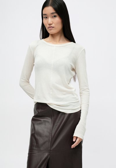 Top de manga larga en tela ligera color crema, con cuello redondeado y ajuste slim, acompañado de una falda de cuero marrón oscuro con abertura.