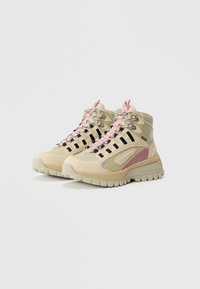 Zapatillas altas en color beige y rosa con suelas robustas, ojetes en negro y ganchos para los cordones en plata, posicionadas una al lado de la otra sobre un fondo liso.