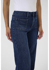 Tumesinised teksapüksid kõrge vöökohaga, millel on kaks tagataskut ja sirged säärised. Riiematerjalil on peen tekstuur.