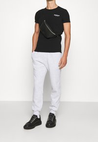 Svart åtsittande t-shirt med logga, grå sweatpants med elastiska muddar och svarta sneakers med dekorativa öljett.