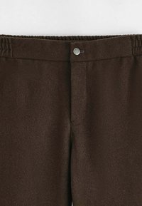 Pantalon en tissu brun à texture lisse, doté d'une ceinture élastique et d'une fermeture à bouton-pression argenté à l'avant.