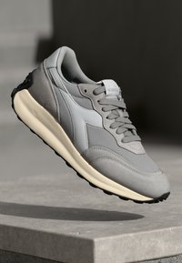 Baskets de course grises avec une tige en mesh, des accents en daim et une semelle intermédiaire de couleur crème. Le design comprend des lacets et une semelle extérieure texturée noire.