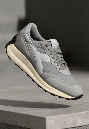 Gray running shoe featuring a mesh upper, suede accents, and a cream-colored midsole. The design includes laces and a textured black outsole.