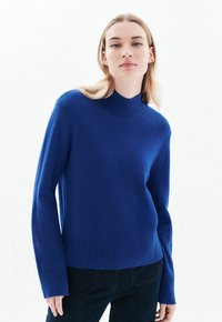 Blauwe gebreide trui met een hoge ribbels boord, lange mouwen en ribbels onderrand. Zachte textuur met een getailleerde pasvorm.