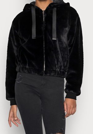 Black plush zip-up hoodie with ribbon drawstrings worn by person in ripped black pants, centered upper body view against plain background.