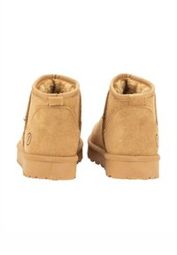 Botines de ante color arena con un suave forro interior, tacón bajo y parte trasera texturizada, que cuentan con una suela de goma plana y un logotipo de la marca en el costado.