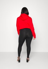 Rode hoodie gecombineerd met zwarte leggings met witte zijstrepen, gedragen met zwarte hakken. Zachte textuur, casual ontwerp.