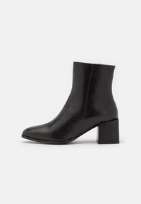 Černé kožené kotníkové boty s špičatou špičkou a stohovaným čtvercovým podpatkem. Hladká textura s minimálními švy.