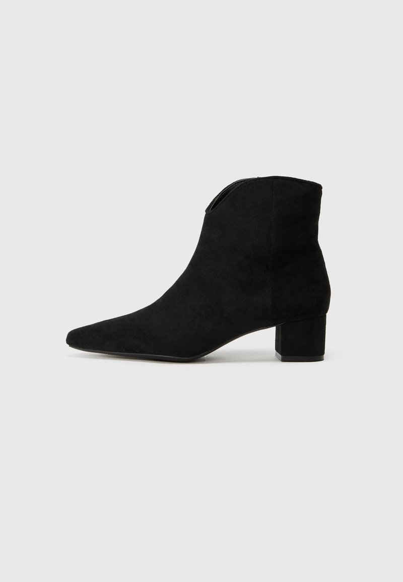 Bottine en daim noir avec bout pointu et petit talon bloc sur un fond clair uni.