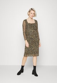 Vestido de estampado de leopardo com decote quadrado e mangas longas transparentes, feito de tecido leve, combinado com botas pretas até ao tornozelo.