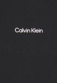 Camiseta de algodón negra con el logo "Calvin Klein" en blanco, en una tipografía minimalista centrada en el área del pecho, textura suave.