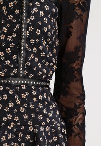 Blumendruckkleid mit schwarzem Hintergrund, strukturierten Spitzenlangen Ärmeln und silberfarbenen Nietenakzenten entlang des Ausschnitts und der Taille.