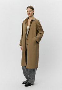 Világosbarna, hosszú kabát nagy gallérral, elülső gombokkal és oldalsó zsebekkel. Szürke, bő szárú nadrág és sötét cipő felett viselve.