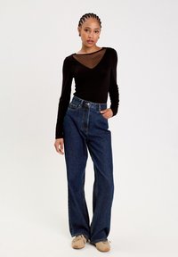 Haut noir à manches longues avec encolure transparente à pois, associé à un jean large en denim bleu taille haute et des baskets beiges.