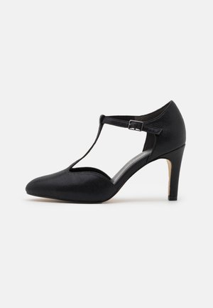 Chaussure à talon haut fermée pour femmes noires avec bride en T, boucle réglable et talon effilé de hauteur moyenne sur fond blanc.