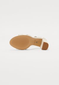 Sandal con tacco alto beige con suola in gomma testurizzata, dotata di una fascia trasparente e di un tacco quadrato. Nome del brand "ALDO" inciso.
