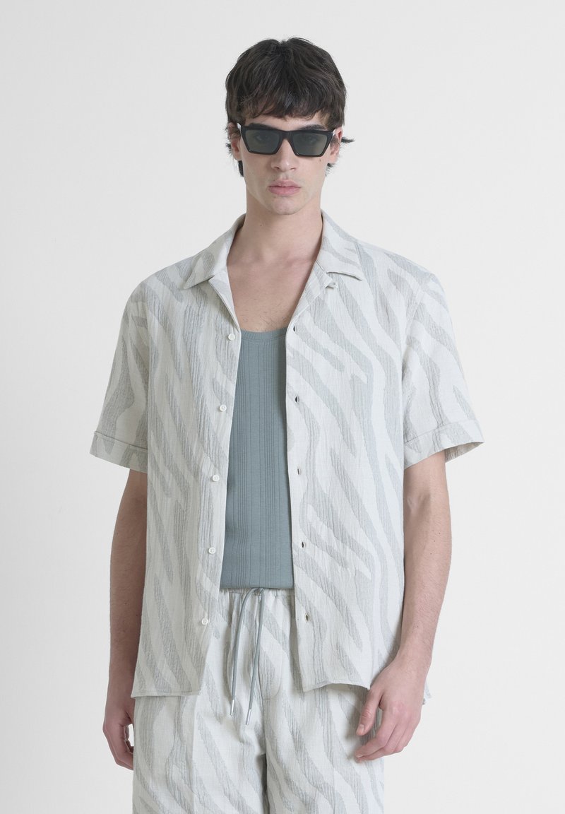 Camicetta bianca a maniche corte con stampa zebra grigia, abbinata a una canotta azzurro chiaro e pantaloni corti coordinati, caratterizzati da un taglio morbido e chiusura con bottone.