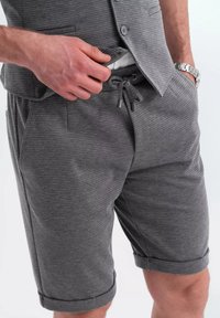 Pantaloni corti grigi con texture, cintura con cordoncino, orlo risvoltato e tasche laterali. Il tessuto presenta un motivo sottile per un tocco di dettaglio in più.