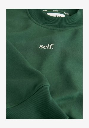 Zielona bluza z miękkiego materiału, z prążkowanym kołnierzem i mankietami. Na przodzie haftowane białe logo "self.".