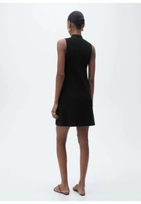 Black sleeveless knit dress with a high neckline, fitted silhouette, and a flared hem, paired with light brown sandals.