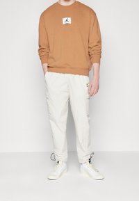 Brun sweatshirt med en åtsittande halsringning och vit logotyp-patch. Löst sittande vita cargo-byxor med sidofickor. Vita sneakers.