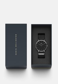 Orologio da polso nero con cassa rotonda in argento e quadrante nero, dotato di sottili indicatori delle ore e un cinturino in nylon nero, presentato in una scatola blu.