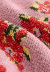 Gebreide stof met een roze achtergrond en rode, gele en groene bloemenpatronen. De textuur lijkt zacht en vlassig.