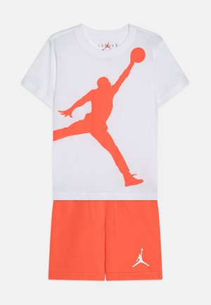 T-shirt blanc avec une grande silhouette graphique orange d'un joueur de basketball. Assorti avec un short orange présentant un accent logo blanc.
