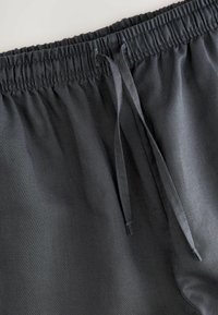 Pantaloni corti grigio scuro con elastico in vita, dotati di un cordino e una texture liscia. Design semplice senza motivi o hardware.