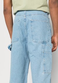 Pantalones cargo de mezclilla de un suave color azul claro con una cintura alta, que cuentan con grandes bolsillos traseros y lazos laterales. Textura suave y diseño de corte holgado.