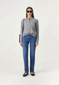 Hallitusseente hall cardigan, sinised sirged teksad ja mustad lamedad kingad. Mudel seisab õlakotiga, kandes päikeseprille. Lihtne, igapäevane riietus.