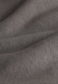 Nahaufnahme von weichem, grauem Strickstoff mit feinen, gleichmäßigen Nähten und sanften Falten im Material.