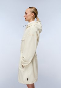 Impermeabile color crema con cappuccio regolabile, tasche con cerniera e maniche elastiche. Presenta una patch del logo sulla parte superiore del braccio.