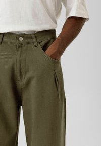 Olijfgroene broek van dikke stof, met knoopsluiting, voorzakken en een comfortabele pasvorm met subtiele plooien.