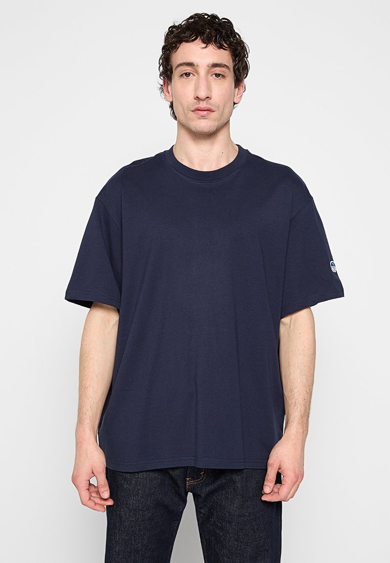 Camiseta de algodón de color azul marino con cuello redondo y mangas cortas, con un corte holgado y un logo sutil en la manga izquierda.