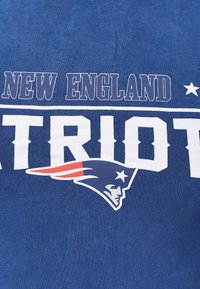 Sininen puuvillapelipaita, jossa lukee "NEW ENGLAND PATRIOTS" rohkeilla valkoisilla kirjaimilla, ja vasemmalla puolella on patriotin pään logo.