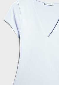 Chemise à manches courtes bleu clair avec col en V et coutures visibles sur les manches, fabriquée à partir d'un tissu doux et lisse.