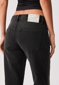 Schwarze Jeans aus Denim mit glatter Textur, hoher Taille, klassischem Fünf-Taschen-Design und auffälligem Markenlabel am Bund.