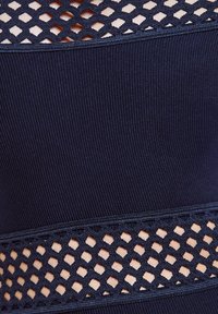 Marineblåt ribbet stof med vandrette udskårne mesh-paneler. Har en tekstureret vævning og foerede detaljer, der skaber en lagdelt visuel effekt.