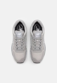 Scarpe da ginnastica grigie realizzate in materiali in mesh e suede, dotate di lacci rotondi, colletto imbottito e un logo bianco sulla linguetta e sul lato.