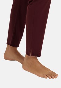 Bordeaux leggings med en tight passform, ankelslitsar och en mjuk textur, i kombination med en bar fot synlig i nedre högra hörnet.