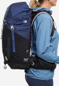 Sac à dos en tissu bleu et noir, avec un design géométrique, des bretelles ajustables, des poches latérales et une ceinture rembourrée pour le soutien.