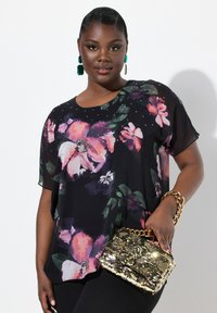 Blusa nera floreale con fiori rosa e viola, maniche corte e scollatura decorata. Borsa dorata con paillettes e tracolla a catena.